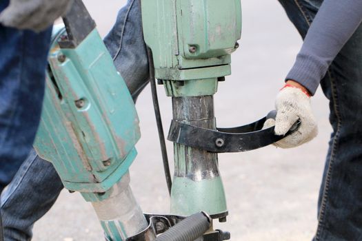 Male workers use electric concrete breaker for digging and drilling concrete repairing driveway surface with jackhammer at the local city road, during sidewalk, work construction site.