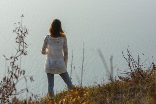 Girl stands on a hill and looks at the sea, rear view