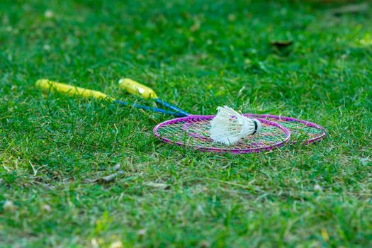On the green grass are badminton rackets and a shuttlecock
