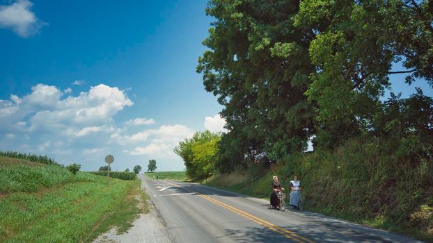 Ronks, Pennsylvania, July 2020 - 2 Amish Women Riding Scooters on a Road on a Summer Day