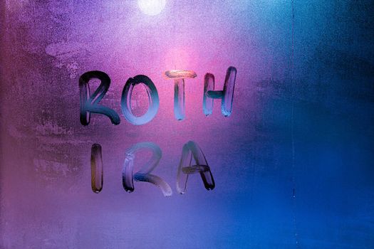 the words roth ira - individual retirement account - handwritten on night wet window glass surface. Idea was proposed by Senator William Roth.