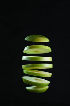Sliced green apple levitates on black background.
