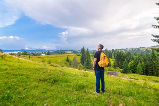 A guy travels with a yellow backpack through picturesque places with beautiful mountain landscapes.