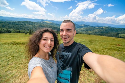 Young couple hugs and take selfie with amazing mountain landscape background.