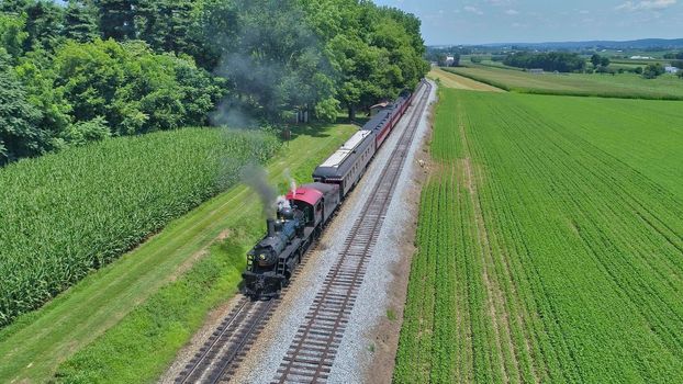 Aerial View of a Restored Antique Steam Engine and Passenger Cars Steaming Up at a Small Rail Road Station on a Summer Day