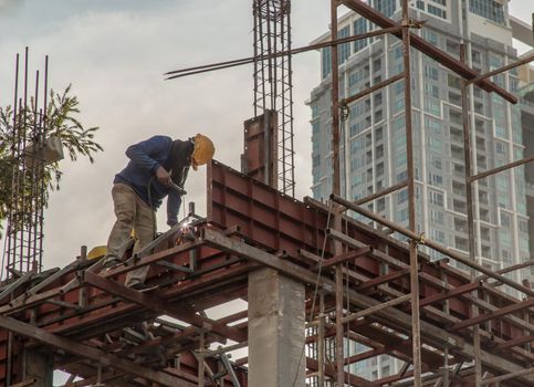 Construction Worker Welding soldering metal girders and Sparks in a Structure high above at the Construction site. Selective focus.