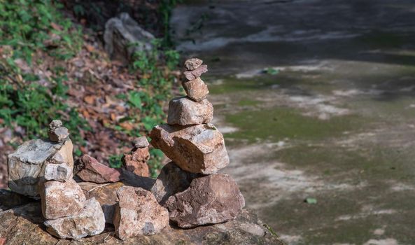 Balanced stone tower on walkway up the mountain with green plants in the background. No focus, specifically.