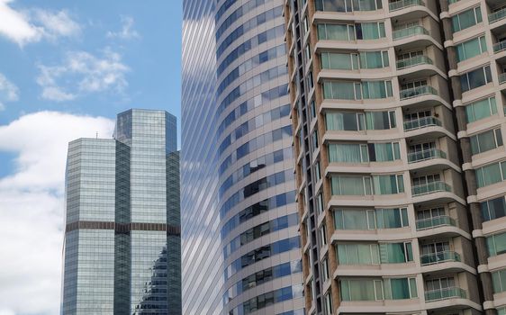 Bangkok, Thailand - July 10, 2019 :  Angular geometric mirror cladding on a modern building with repeating structure and reflected sky and clouds. No focus, specifically.