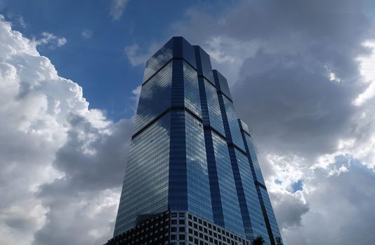 Bangkok, Thailand - July 10, 2019 :  Angular geometric mirror cladding on a modern building with repeating structure and reflected sky and clouds. No focus, specifically.