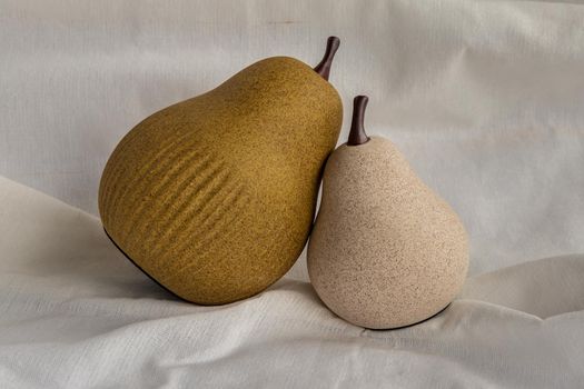 Two ceramics pear fruits on white fabric background. Ceramic tableware, Home decor.