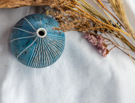Beautiful small blue ceramic vase and Dried flowers on White fabric background. Ceramic tableware, Home decor. Top view, Copy Space.