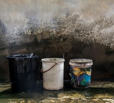 Blue, White and Black Old Plastic Buckets Filled with Rainwater on the cement floor on a rainy day. While it rains, we can take the container over the rainwater to keep it. Save water, save environment concept, Copy space, No focus, specifically.