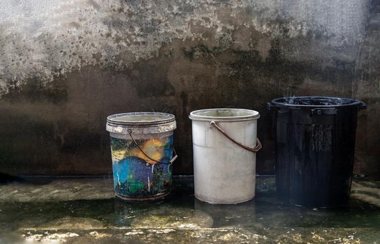 Blue, White and Black Old Plastic Buckets Filled with Rainwater on the cement floor on a rainy day. While it rains, we can take the container over the rainwater to keep it. Save water, save environment concept, Copy space, No focus, specifically.