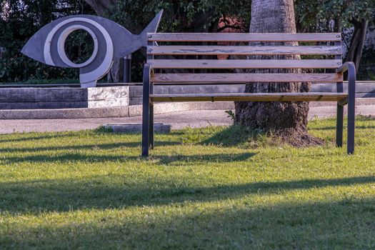 Wooden benches on grass floor in a shady area of the park. Seating and unwind area. Selective focus.