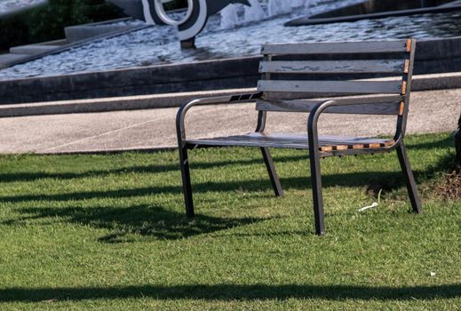 Wooden benches on grass floor in a shady area of the park. Seating and unwind area. Selective focus.