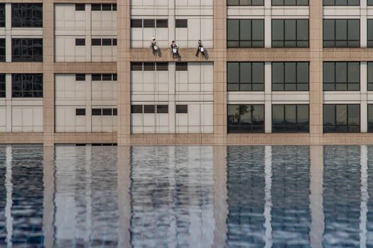Group of workers cleaning windows service on high rise office building with reflection from swimming pool. Selective focus.