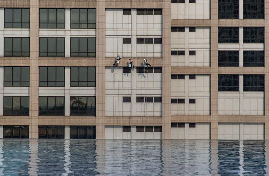 Group of workers cleaning windows service on high rise office building with reflection from swimming pool. Selective focus.