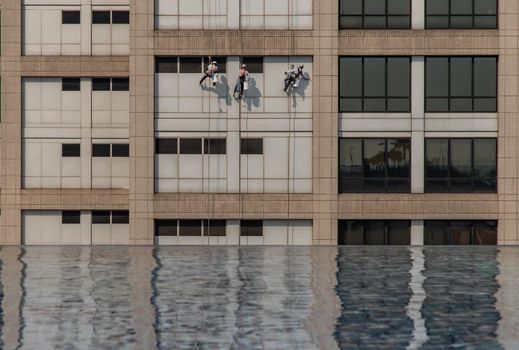 Group of workers cleaning windows service on high rise office building with reflection from swimming pool. Selective focus.
