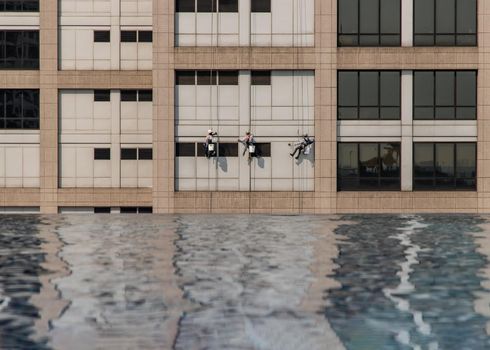Group of workers cleaning windows service on high rise office building with reflection from swimming pool. Selective focus.
