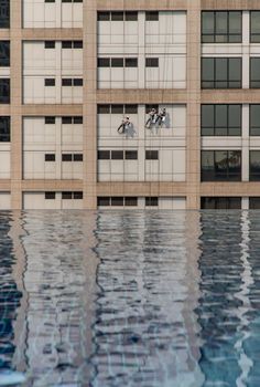 Group of workers cleaning windows service on high rise office building with reflection from swimming pool. Selective focus.