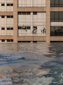 Group of workers cleaning windows service on high rise office building with reflection from swimming pool. Selective focus.