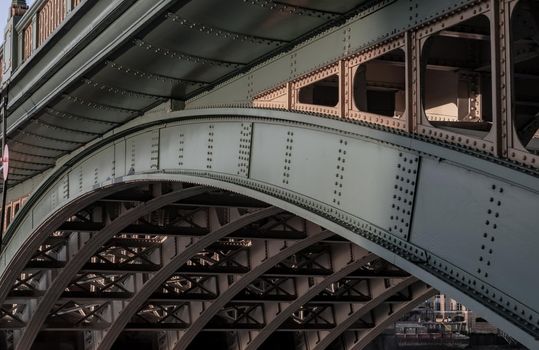 London, England - Apr 20, 2019 : Side view of Beams and Rivets-structure under the Bridge span in the setting sun. Large metal bridge over water, No focus, specifically.