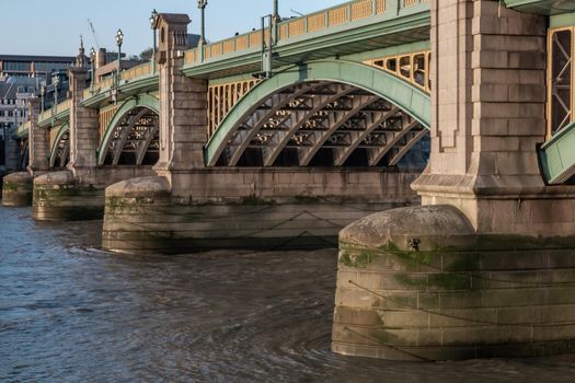 London, England - Apr 20, 2019 : Side view of Beams and Rivets-structure under the Bridge span in the setting sun. Large metal bridge over water, No focus, specifically.