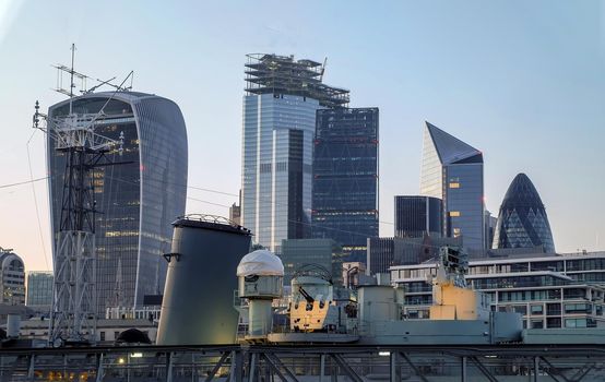 London, England - Apr 20, 2019 : HMS Belfast museum ship moored on the River Thames with modern high-rise buildings in the background. City skyline, No focus, specifically.