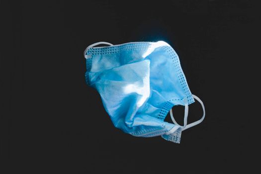 Protective face mask made of blue plastic, on a dark background, wrinkled, dirty and discarded, symbol of the health decadence and the global crisis of the COVID-19 pandemic.