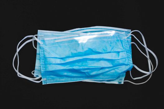 Protective face mask made of blue plastic, on a dark background, wrinkled, dirty and discarded, symbol of the health decadence and the global crisis of the COVID-19 pandemic.
