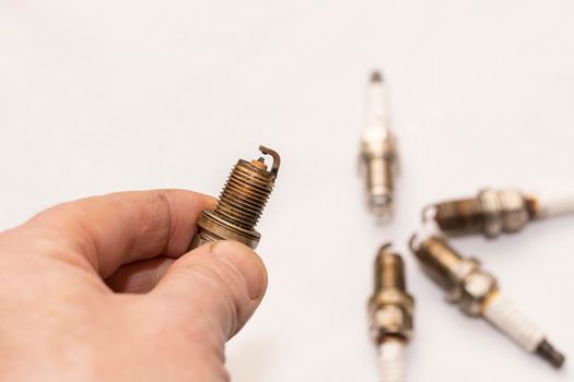 a man's hand holds an old worn out gasoline car spark plug on an empty clean white background