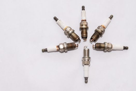 a set of old worn out petrol car spark plugs lie next to one new one on a blank clean white background