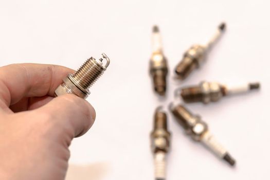 a man's hand holds a gasoline car spark plug against a background of worn-out old used-up, resource parts on an empty clean white background