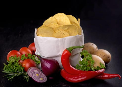 Potato chips on a dark wooden board. Fast food. Dark background. Top view