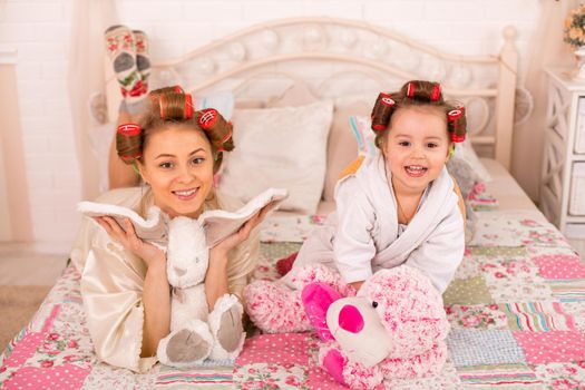 A charming little girl with her mother in hair curlers are having fun. Women's Day. Girl having fun with mom.