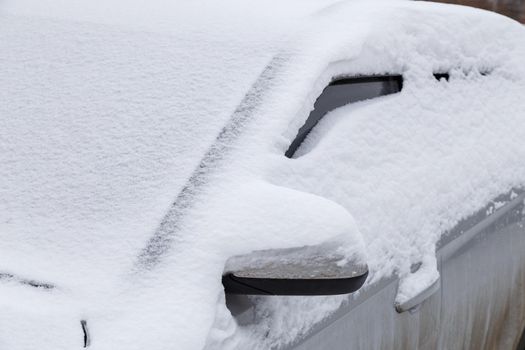 silver car covered with thick layer of snow at cloudy day light - close-up with selective focus