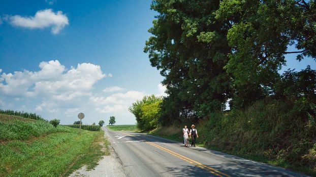 Ronks, Pennsylvania, July 2020 - An Amish Couple One Walking and One on a Scooter on a Road on a Summer Day