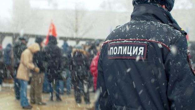 Two cops at a demonstration under the snowfall. Protest rally against construction, for maintaining parks. Text on jacket - police