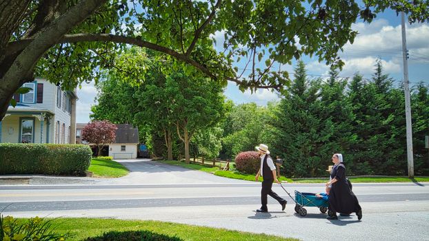 Gordonville, Pennsylvania, June 2020 -An Amish Family Walking along a Country Road Pulling a Wagon with a Small Child in it