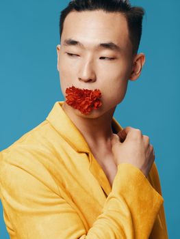 Sexy man with a red flower in his mouth on a blue background yellow jacket model Asian appearance. High quality photo