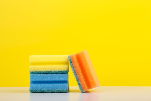 Horizontal still life with colorful sponges for washing dishes on white table against yellow background with copy space. High quality photo