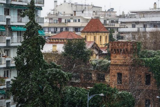 Snow falling on residential area with blocks of flats surrounded be trees.