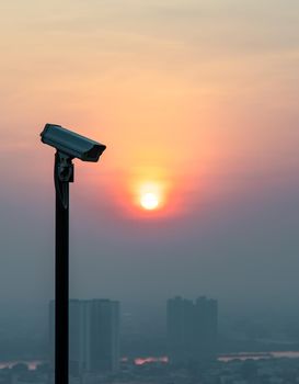 Modern surveillance camera on cityscape and skyscraper background with sun shing bright before the sun was setting. The concept of surveillance evening time, copy space, Selective focus.