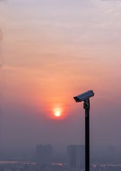 Modern surveillance camera on cityscape and skyscraper background with sun shing bright before the sun was setting. The concept of surveillance evening time, copy space, Selective focus.