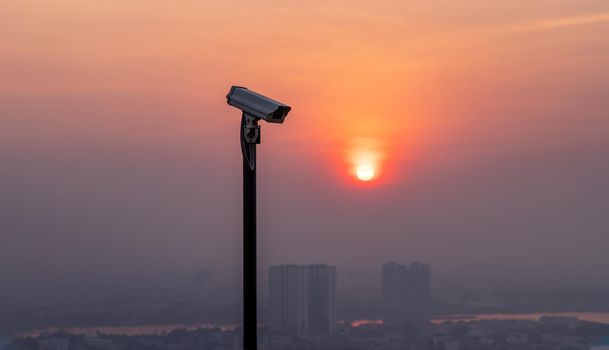 Modern surveillance camera on cityscape and skyscraper background with sun shing bright before the sun was setting. The concept of surveillance evening time, copy space, Selective focus.