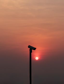 Modern surveillance camera in the foreground The orange sun shing bright before the sun was setting. The concept of surveillance evening time, copy space, Selective focus.