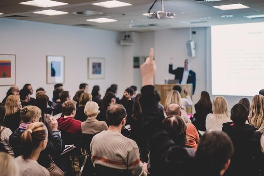 I have a question. Group of people sitting at the chairs in conference hall, raising their hands. Workshop at university. Business and Entrepreneurship event.