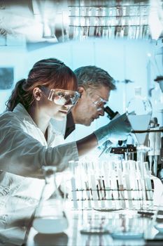 Health care researchers working in life science laboratory. Young female research scientist and senior male supervisor preparing and analyzing microscope slides in research lab.