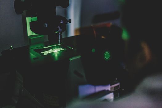 Life science female researcher microscoping with hi-tech fluorescent microscope in scientific genetic laboratory. Healthcare and biotechnology.