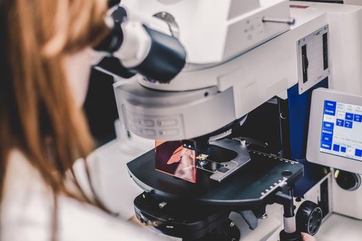 Female scientist microscoping on hi-tec fluorescent microscope. Health care professional in hes working environment.